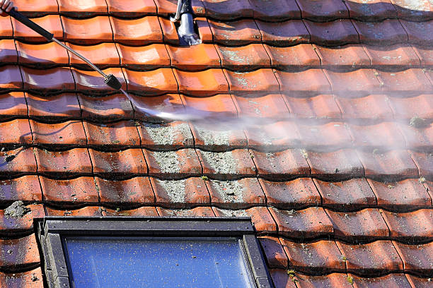Worker is Démoussage toiture à Bouguenaisthe roof and rainwater gutter with high pressure. Démoussage toiture à Bouguenais